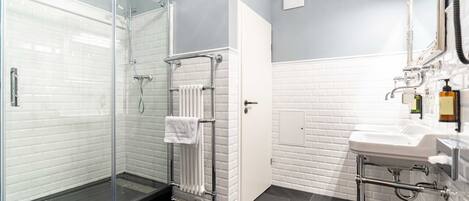 Un baño moderno con ducha de vidrio, pared con azulejos blancos, piso de azulejos negros y lavamanos blanco con accesorios cromados.