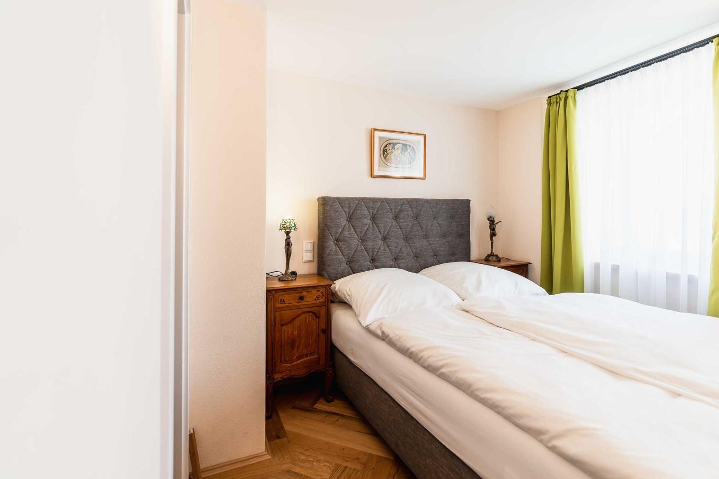 A bedroom with a large bed, a nightstand, a lamp, and a framed picture on the wall.