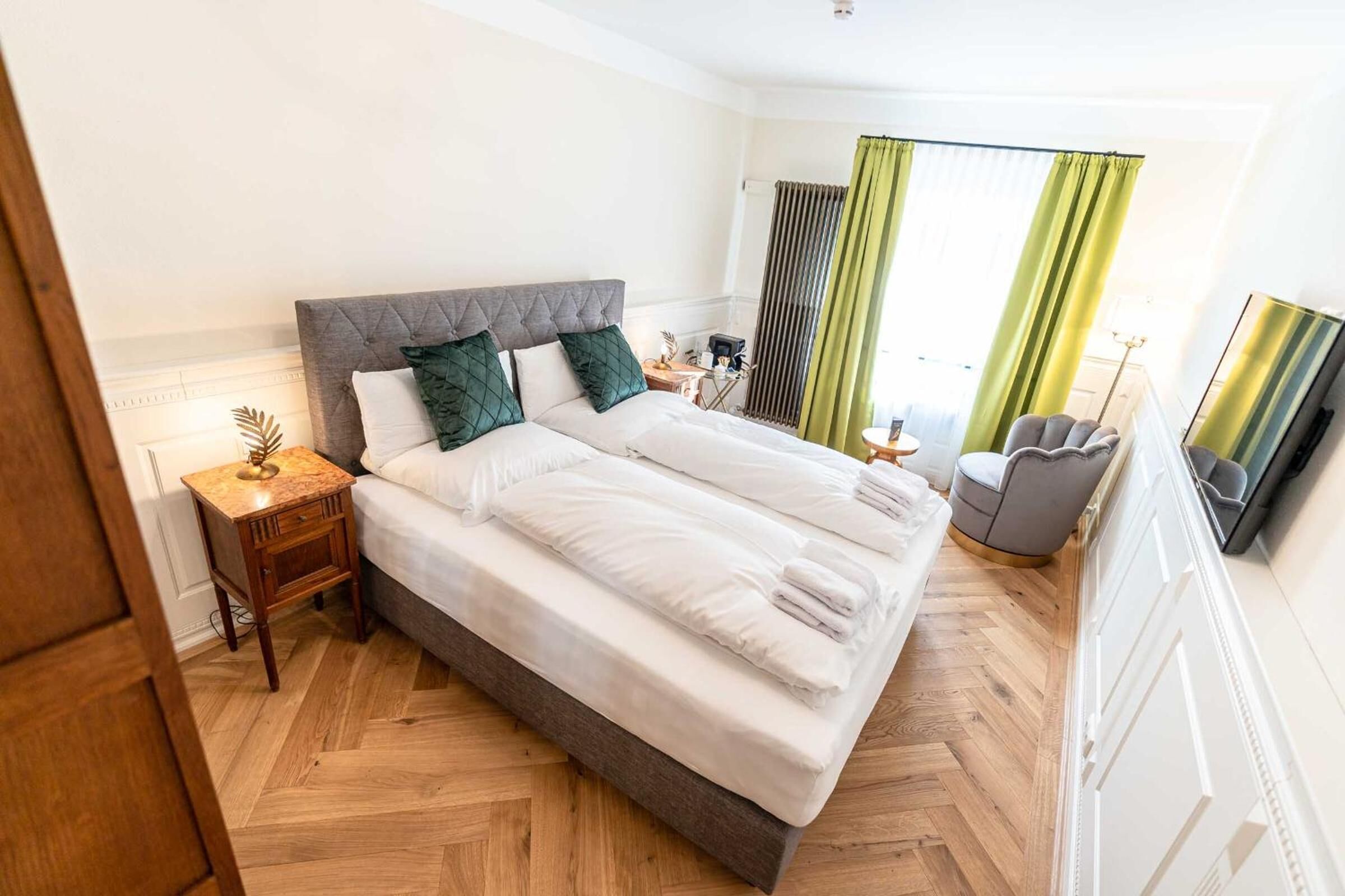 A neatly arranged hotel room with a large bed, a bedside table, a chair, and a mirror.