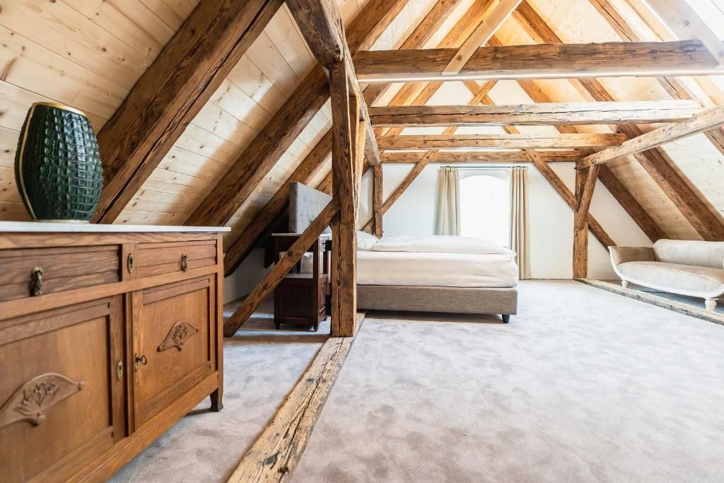 Ein Schlafzimmer mit schrägen Wänden, Holzbalken, einem Bett, einer Kommode und einem Fenster.