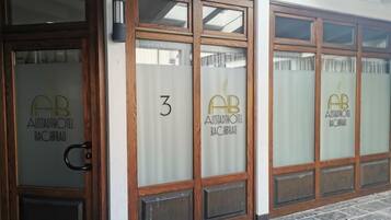 Exterior de un hotel con puertas de madera y ventanas con vidrio esmerilado, cada una identificada con el nombre y logotipo del hotel.