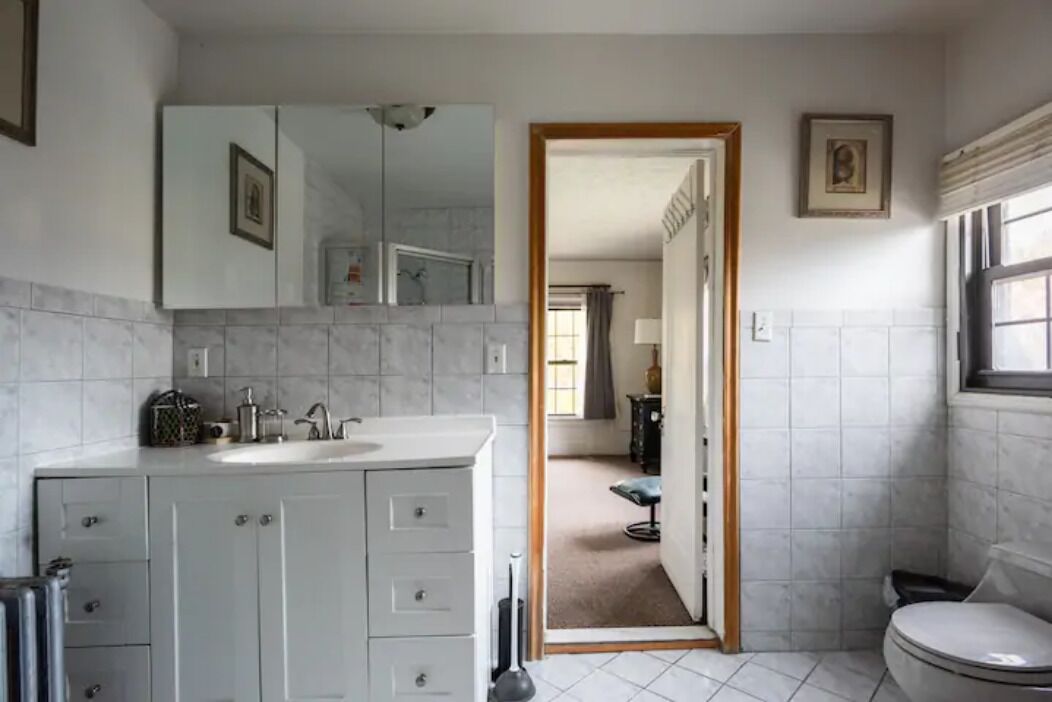 A bathroom with a white sink, mirror, and toilet, and a doorway leading to another room.