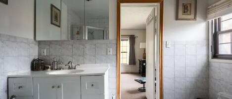 A bathroom with a white sink, mirror, and toilet, and a doorway leading to another room.