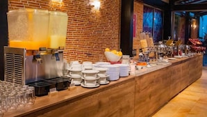 A breakfast bar with a brick wall, a juice dispenser, and various breakfast items. - Best Western Plus Hotel San Diego (Medellín)