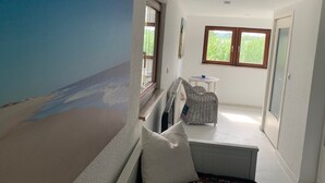 Una habitació amb una finestra gran, una taula petita, una cadira de vimet i un radiador.