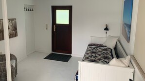 Habitació petita i ordenada amb un llit individual, una tauleta de nit, una làmpada de paret i una porta amb una finestra.