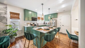 Une cuisine moderne avec des meubles de couleur verte, un îlot central doté de tabourets de bar et un éclairage suspendu.
