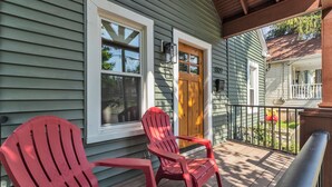 Une véranda avec deux fauteuils Adirondack rouges, une porte en bois et une fenêtre à cadre blanc.