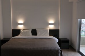 A modern hotel room with a large bed, two bedside tables, and a view through a sliding glass door.