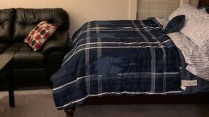 Ein Schlafzimmer mit einem Bett, einer schwarzen Ledersofa, einem Deckenventilator und einem Fenster mit Jalousien.
