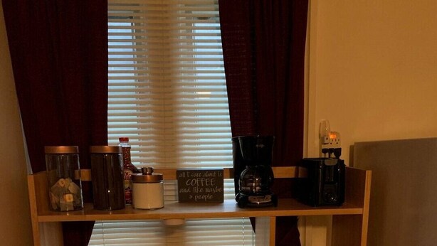 Eine kleine Küche mit einem Holztisch, einer Kaffeemaschine und einem Schild mit der Aufschrift: 'Alles, was zählt, ist Kaffee – und vielleicht ein paar Menschen'.