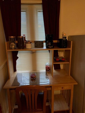 A compact kitchen with a wooden table, a coffee maker, and a sign stating "all I care about is coffee and like maybe a people."