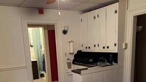 Eine kleine Küche mit weißen Schränken, einer schwarzen Arbeitsplatte und einem Deckenventilator aus Holz.