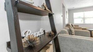 A modern living room with a dark wooden shelf displaying decorative items and a 'Beach' sign.