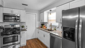 A modern kitchen with white cabinets, stainless steel appliances, and a granite countertop.