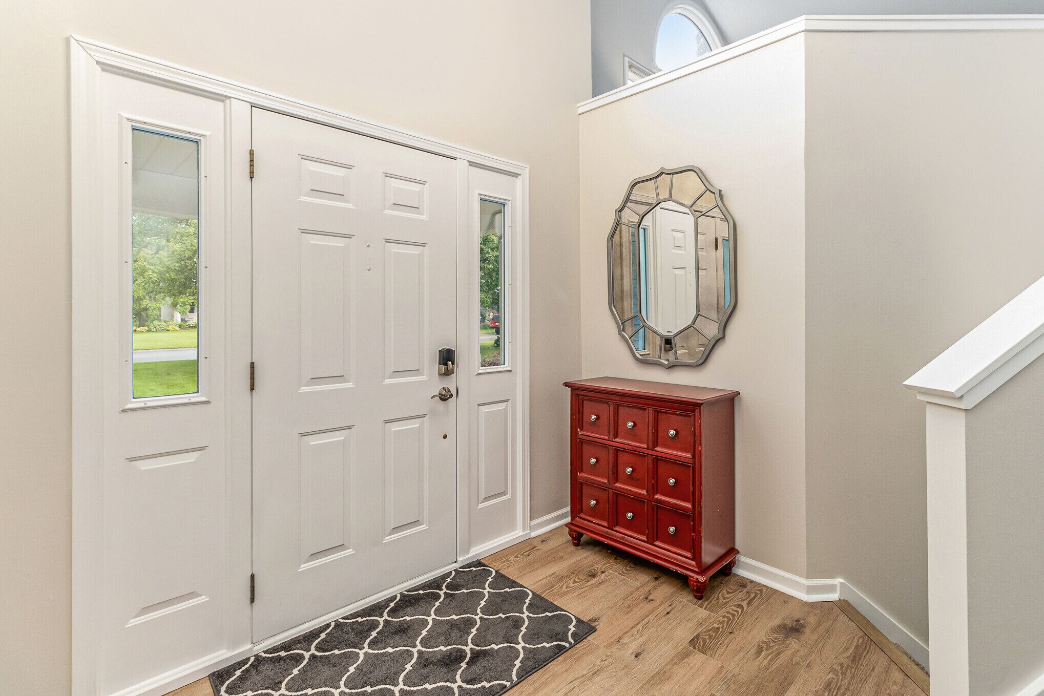 A hallway with a white door, a red dresser, and a mirror on the wall.