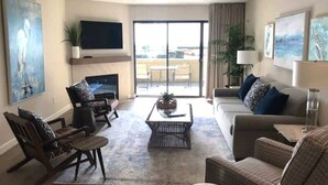 A living room with a sofa, chairs, a coffee table, a flat-screen TV, and a balcony with a view.