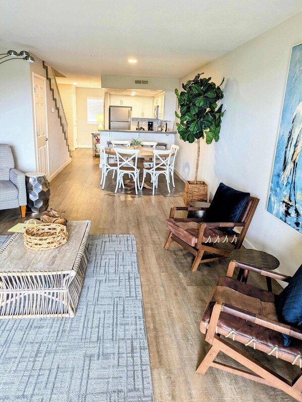 Un vaste salon comprenant un coin repas, une cuisine à l’arrière-plan et un escalier menant à un autre niveau.