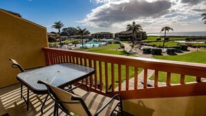 A balcony with a table and chairs, overlooking a pool and resort buildings.
