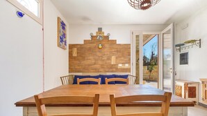 Un comedor con una mesa y sillas de madera, una pared decorativa con un colgador de luz y vista a un área exterior a través de una puerta abierta.