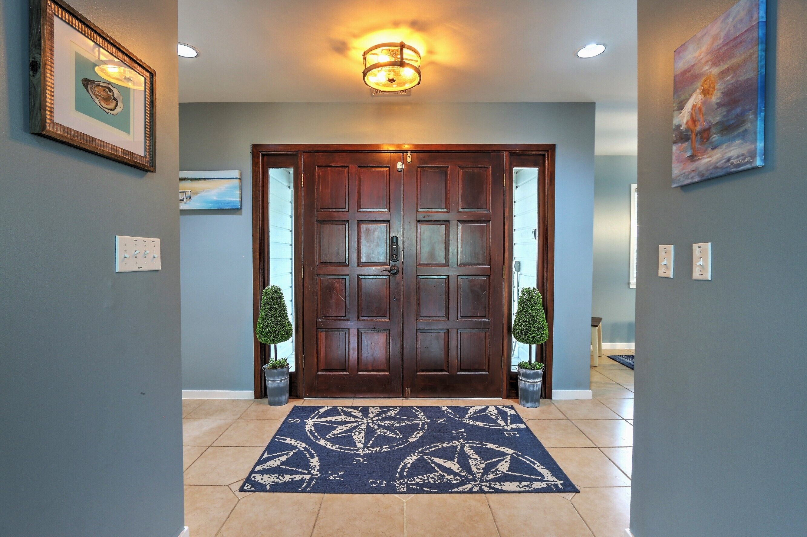 A hallway with a wooden double door, a blue patterned rug, and two potted plants on either side.