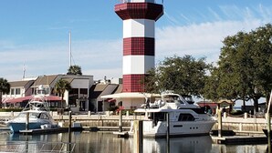 Ein Leuchtturm mit einem rot-weiß gestreiften Turm, ein Jachthafen mit Booten und ein Gebäude mit rotem Dach im Hintergrund.