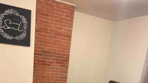 A living room with a black leather sofa, a wooden coffee table, and a brick accent wall. - Stocked home close to Yale, in Heart of New Haven (New Haven)