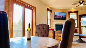 A dining area with a round table, a bottle of wine, and a television mounted on the wall.