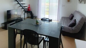 Ett modernt vardagsrum med matplats, soffa, trappa och utsikt genom stora fönster.