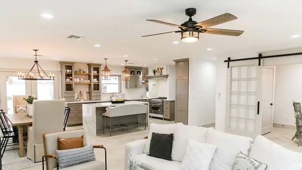 A modern kitchen with a central island, a dining area with a wooden table, and a living room with a white sofa and coffee table.
