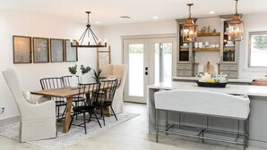 A modern kitchen with a central island, pendant lighting, and a dining area with a wooden table and chairs.