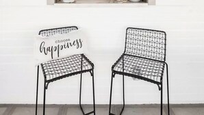 Two black metal chairs with a wireframe design, a sign with the words "choose happiness," and two wall-mounted lanterns with lit candles.