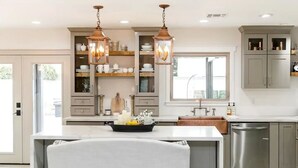 A modern kitchen with a central island, pendant lighting, and built-in shelving.