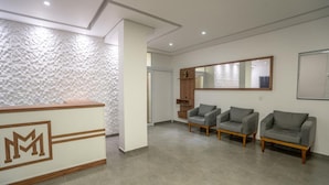 Un área de recepción con mostrador, tres sofás grises, un espejo grande y una pared con textura.