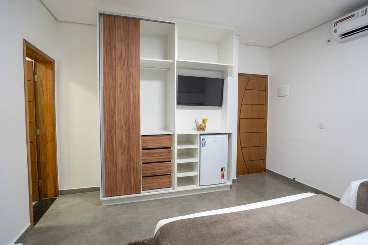 Un dormitorio con armario, televisión, refrigerador pequeño y cama.
