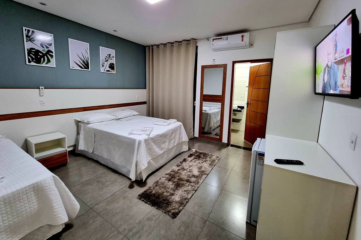 Habitación de hotel con dos camas, televisión, aire acondicionado y baño visible a través de una puerta abierta.