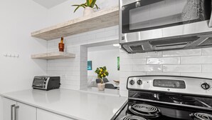 Een moderne keuken met witte kastjes, een ingebouwde magnetron, een fornuis met vier branders en een broodrooster.