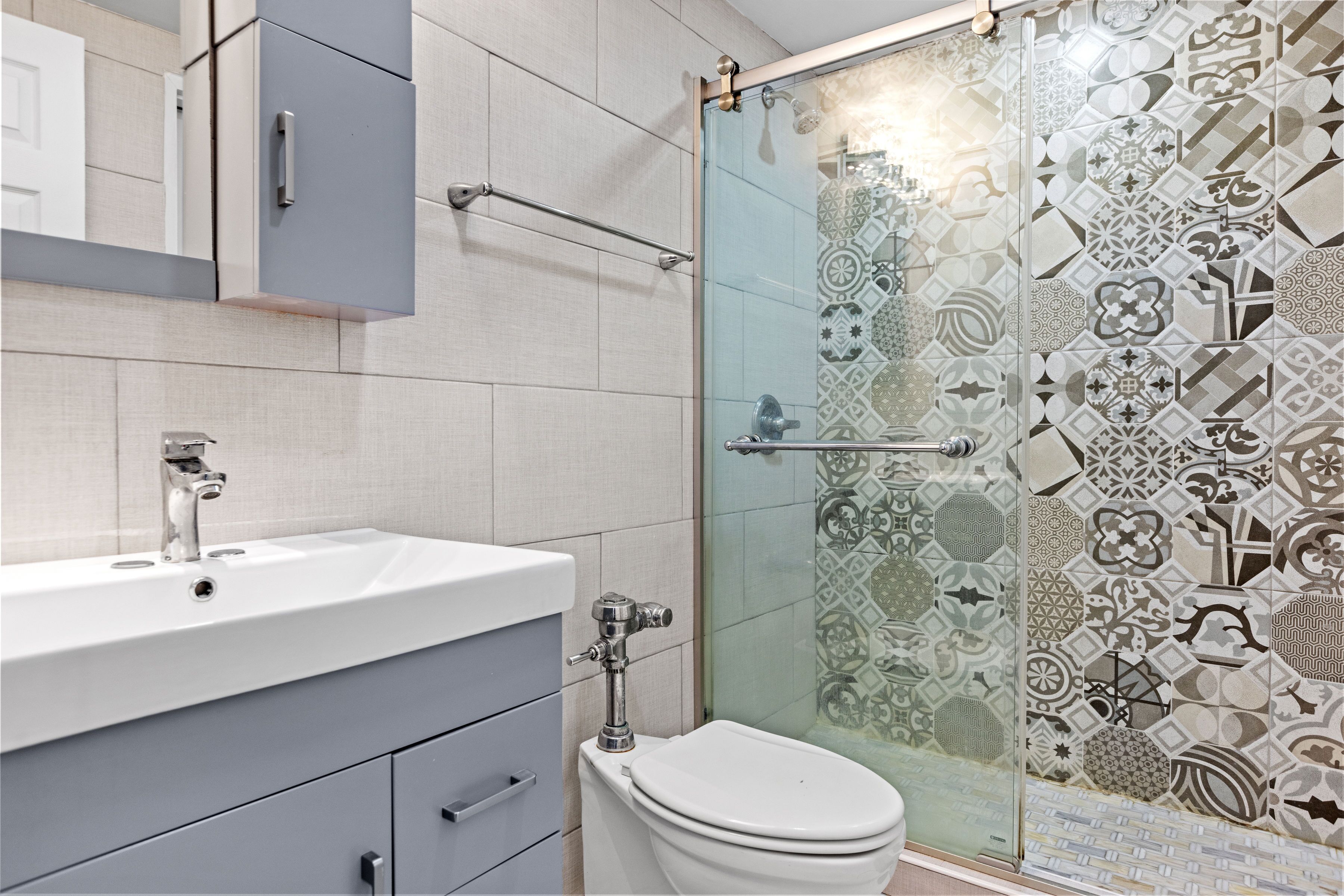 A bathroom with a modern sink, toilet, and a glass shower enclosure with patterned tiles.