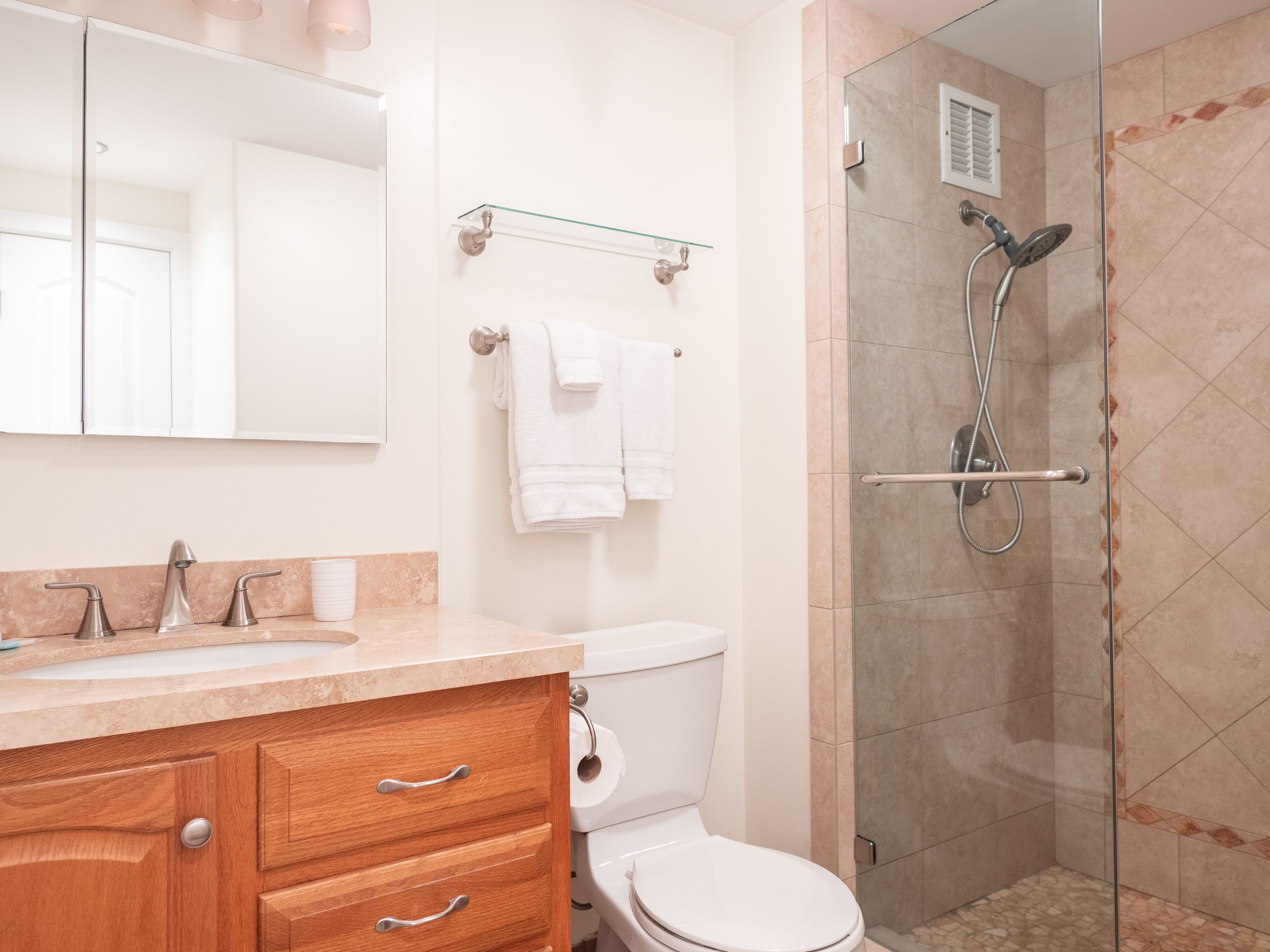 A modern bathroom with a glass-enclosed shower, a wooden vanity with a sink and mirror, and a toilet.