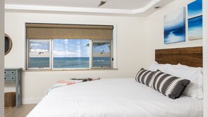 A bedroom with a large bed, a ceiling fan, a window with a view of the ocean, and a wooden headboard.