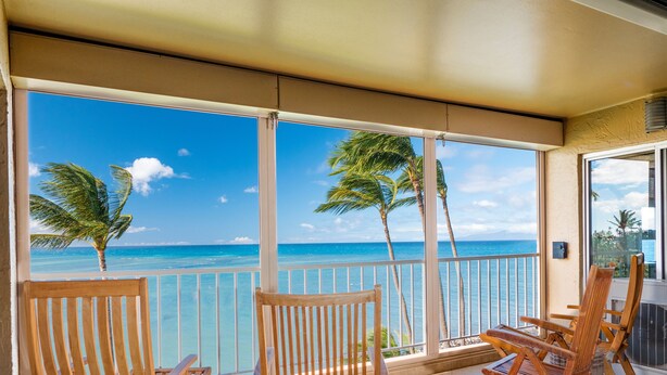 A balcony with wooden chairs and a view of the ocean.