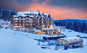 A large, multi-story lodge with a snow-covered roof and multiple balconies, surrounded by a snowy landscape.