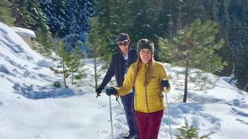 A snowy landscape with two people hiking, surrounded by trees and a clear sky.