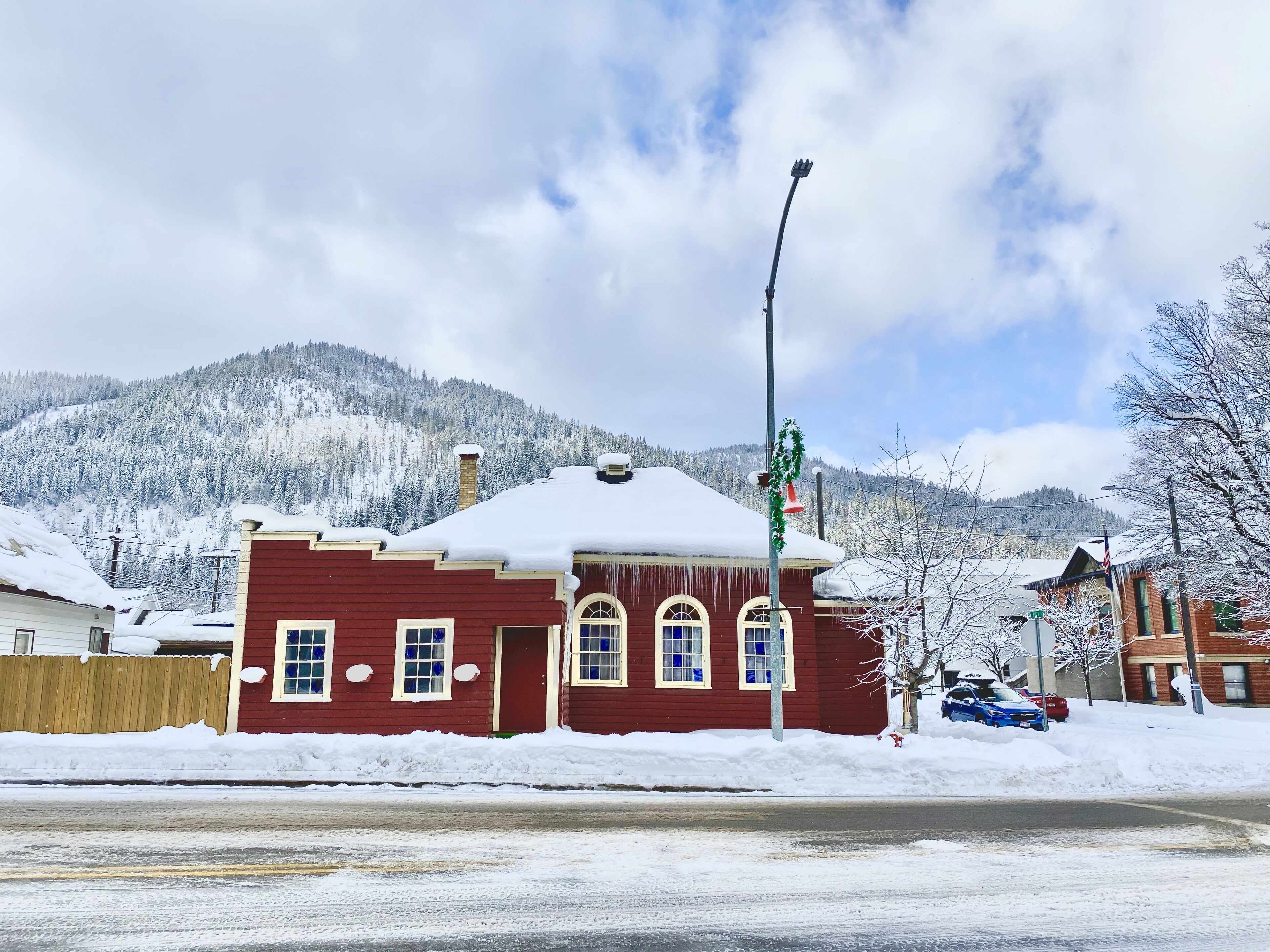 A red building with a snow-covered roof, a street in front, and a mountainous backdrop.
