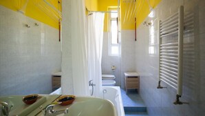 A bathroom with a bathtub, a sink with mirrors, a toilet, and a shower area. - Colorful apt in Milano (Milan)