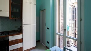 A kitchen with white cabinets, a refrigerator, and a window overlooking a balcony. - Colorful apt in Milano (Milan)