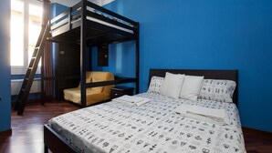A room with a bunk bed, a chair, a bedside table, and a bed with patterned bedding. - Colorful apt in Milano (Milan)