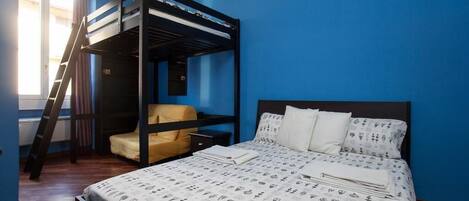 A room with a bunk bed, a chair, a bedside table, and a bed with patterned bedding.