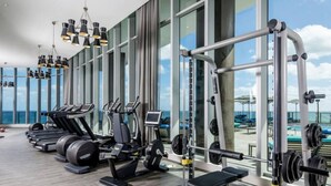 Une salle de sport moderne équipée de machines de cardio, d’appareils de musculation et de grandes fenêtres offrant une vue sur l’océan.