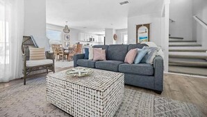 Una sala moderna con un sofá gris, un reposapiés estampado y un comedor al fondo.